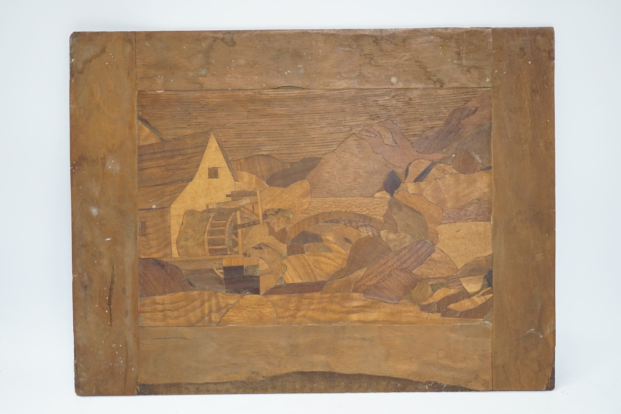 From the Studio of Fred Cuming. An inlaid marquetry panel depicting a watermill before mountains, 30 x 40cm. Condition - poor to fair